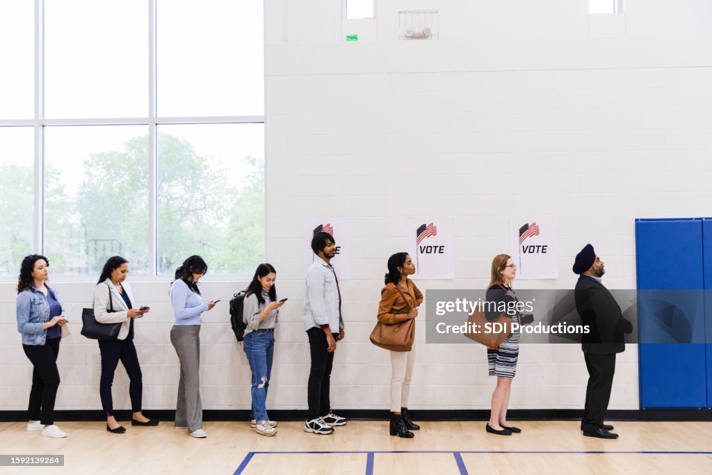 Diverse voters line up along a wall in gym