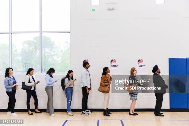 diverse voters line up along a wall in gym - lining up stock pictures, royalty-free photos & images