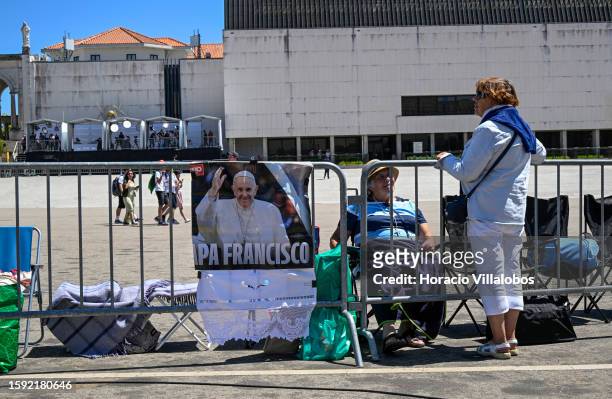 Women chat in front row by Pope Francis poster under a strong sun at the the sanctuary premises as members of the faithful of all ages and...