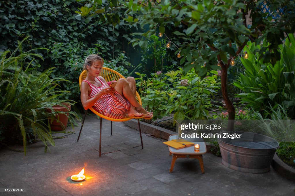 Woman relaxing in garden chair in the evening, using smartphone