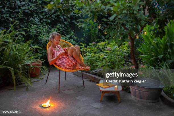 woman relaxing in garden chair in the evening, using smartphone - citrus blossom stock-fotos und bilder