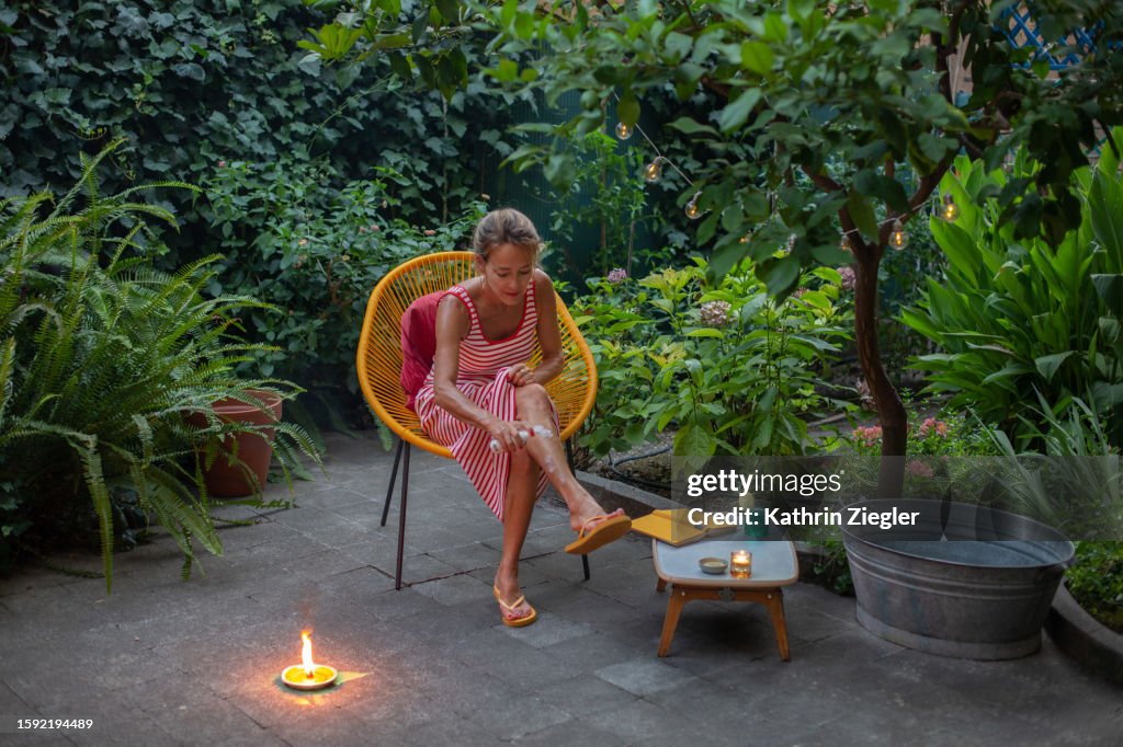 Woman relaxing in garden chair, applying mosquito repellent
