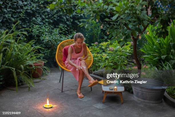 woman relaxing in garden chair, applying mosquito repellent - mug stockfoto's en -beelden
