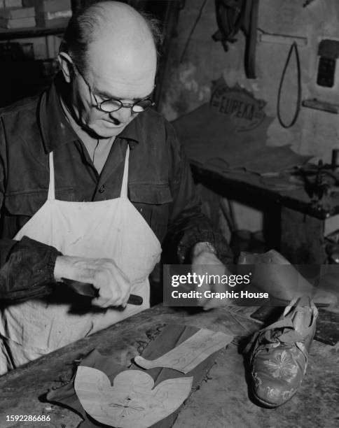 Shoemaker Giuseppe Cottefoglie preparing to cut leather, paper template places over the leather, in his workshop on the Via Leone IV in Rome, Italy,...