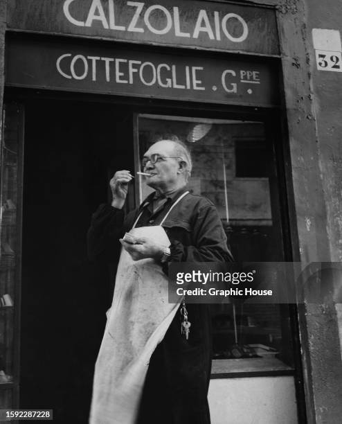 Shoemaker Giuseppe Cottefoglie lighting a cigarette outside his workshop on the Via Leone IV in Rome, Italy, circa 1955.