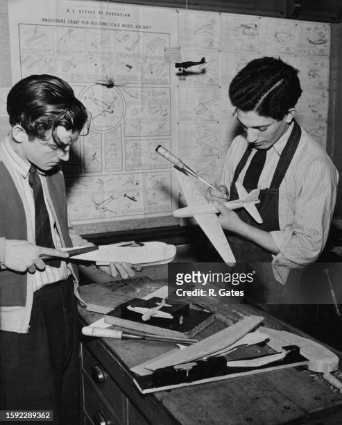 Two students making model aircraft, instruction pinned to the wall read 'US Office of Education, Procedure Chart for Building Scale Model Aircraft',...