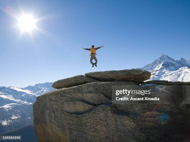 hiker jumps into mid-air from rock summit,arms out - mann freudensprung sonne vorderansicht leger stock-fotos und bilder