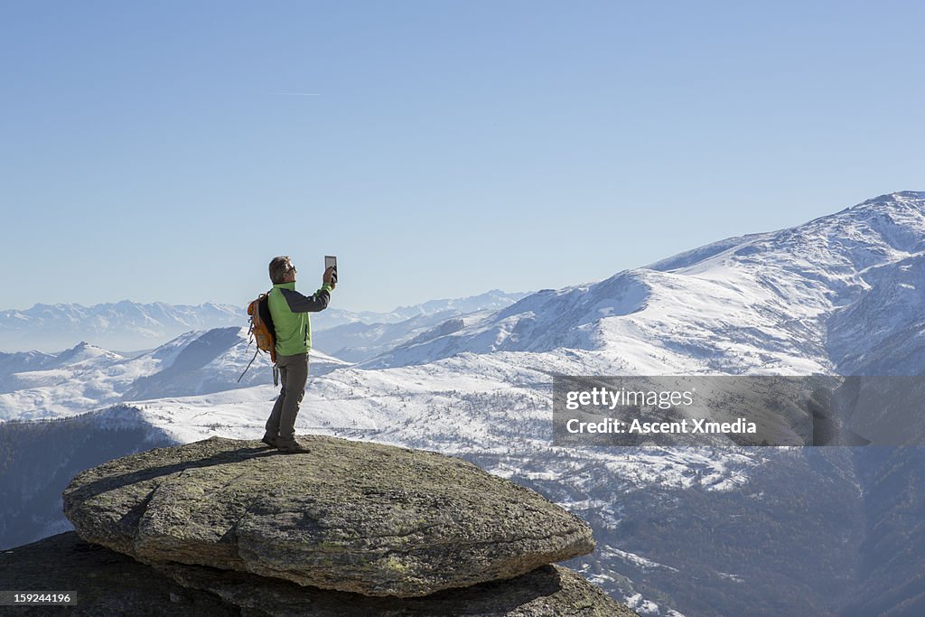 Hiker takes picture with digital tablet, on ummit