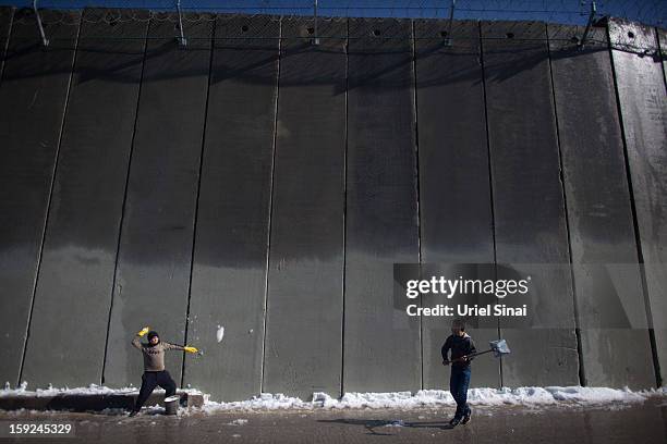 Palestinian children play with snow in front of the controversial Israeli separation barrier on January 10, 2013 in the West Bank village of Abu Dis,...