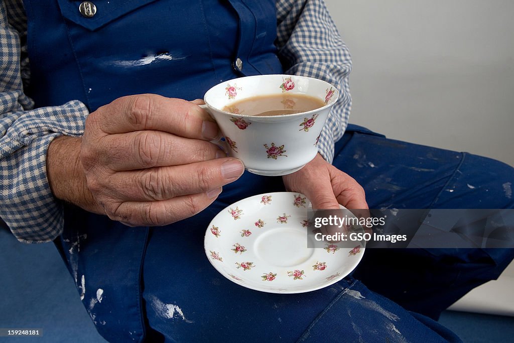 A labourer holds a delicate cup of tea and saucer