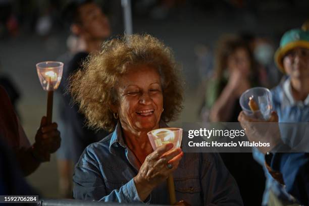 Woman smiles while holding a candle as pilgrims and members of the faithful participate in the Rosary and the Candles Procession at the sanctuary...