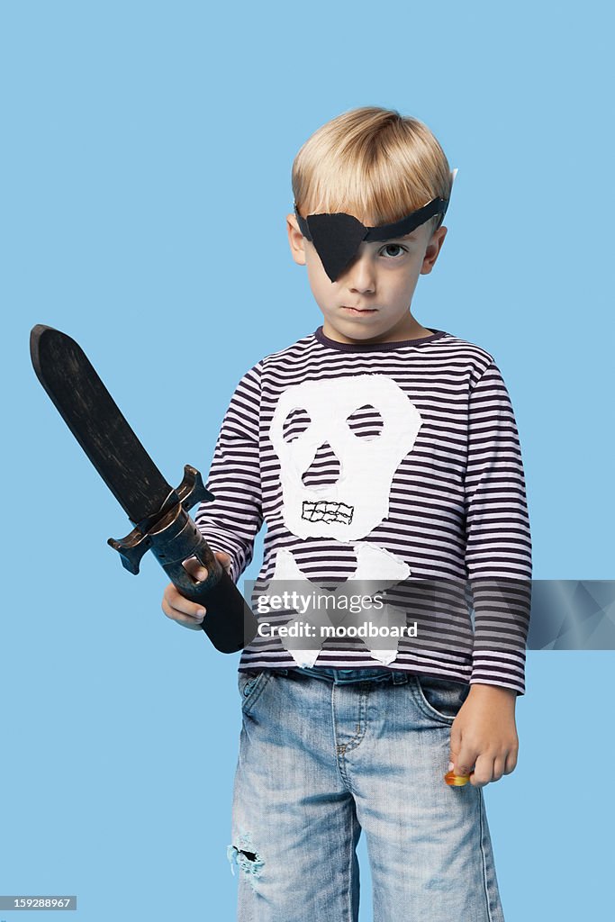 Portrait of a young boy in pirate costume holding sword over blue background