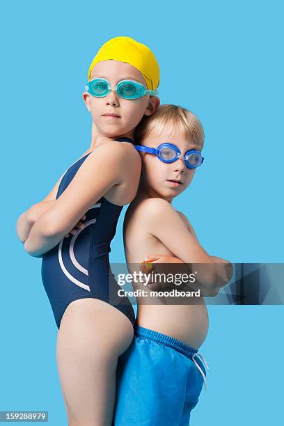 profile shot of young boy and girl in swimwear standing back to back over blue background - studio portrait swimmer photos et images de collection