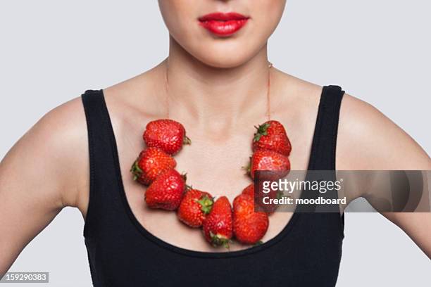 mid section of a woman wearing strawberry necklace over gray background - collana foto e immagini stock