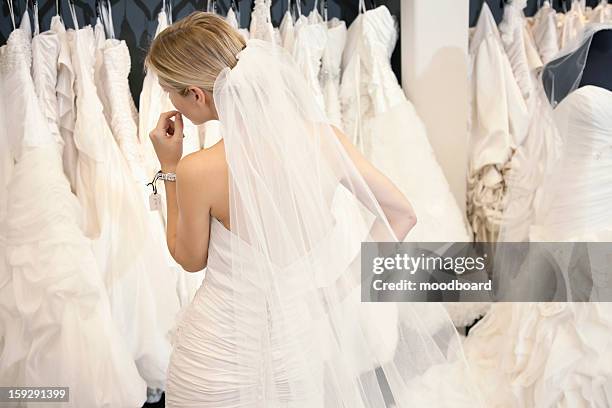 back view of a young woman in wedding dress looking at bridal gowns on display in boutique - robe mariée photos et images de collection