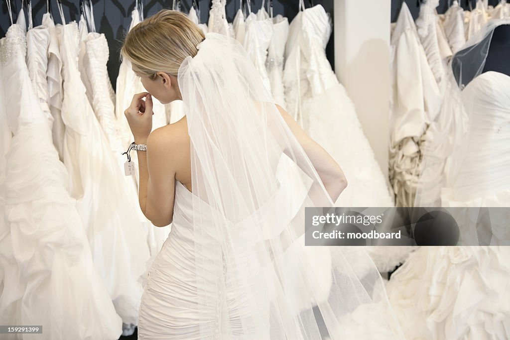 Back view of a young woman in wedding dress looking at bridal gowns on display in boutique