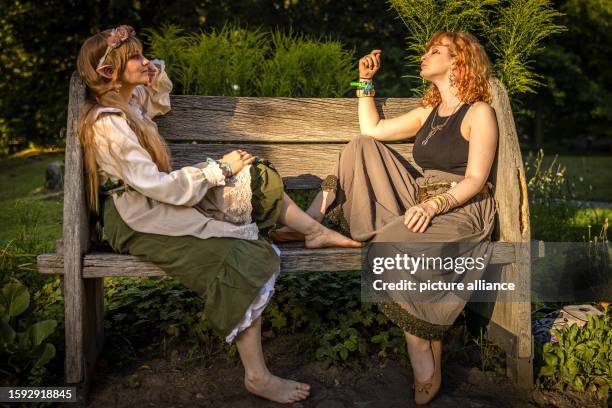 August 2023, Brandenburg, Cottbus: Two participants of the Elbenwald Festival sit on a bench in Spreeauenpark. The Elbenwald Festival is a three-day...