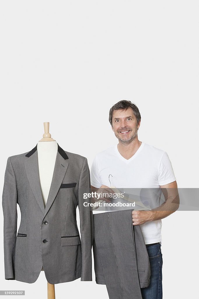 Portrait of mature man standing next to tailor's dummy over gray background