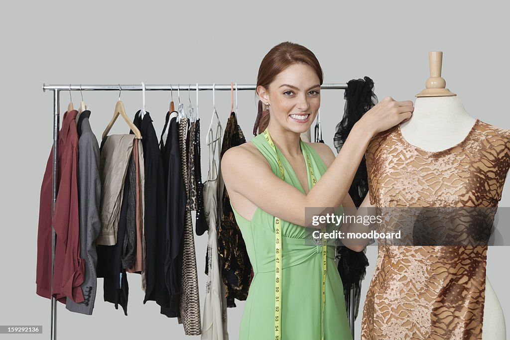 Portrait of beautiful female fashion designer adjusting cloth on tailor's dummy