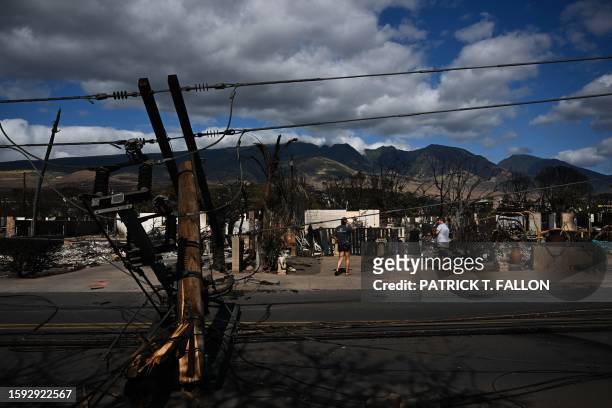 Downed power lines block a road as people feed chickens outside a burnt home in the aftermath of a wildfire in Lahaina, western Maui, Hawaii on...