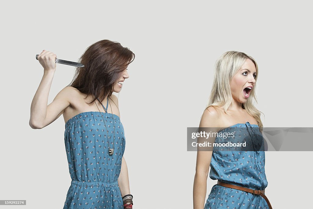 Friend stabbing young woman in similar jump suits from behind
