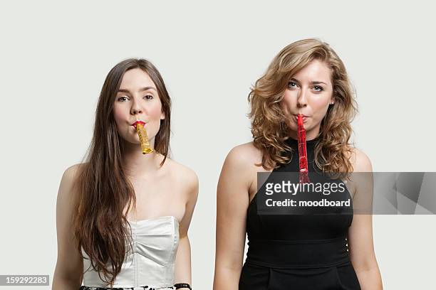 portrait of young women blowing party puffers against gray background - matasuegras fotografías e imágenes de stock