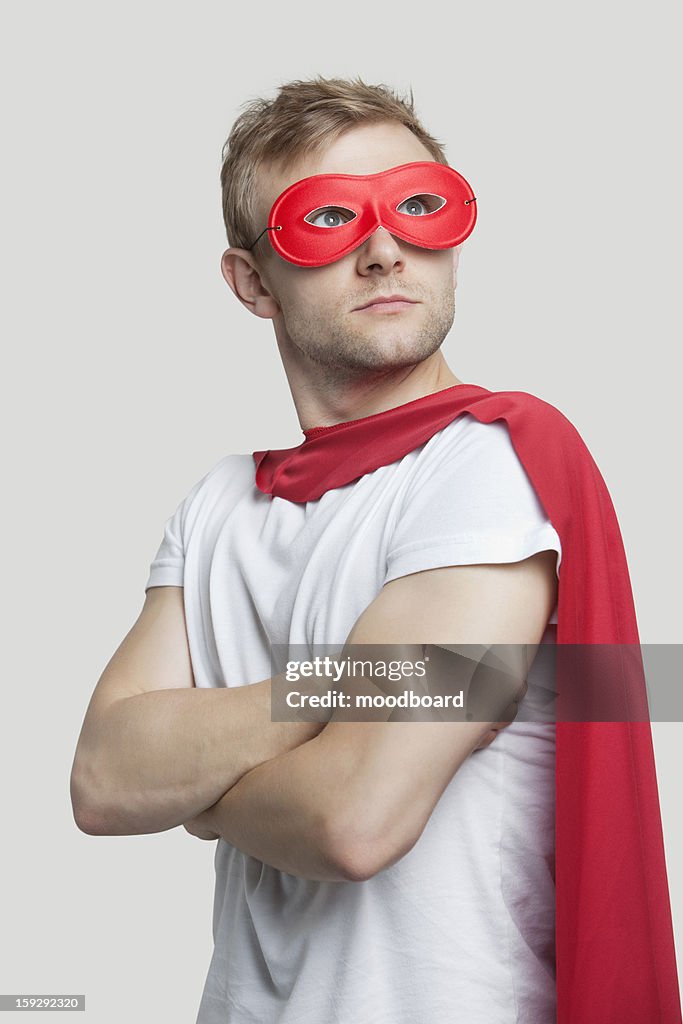 Young man in red superhero costume looking up over gray background