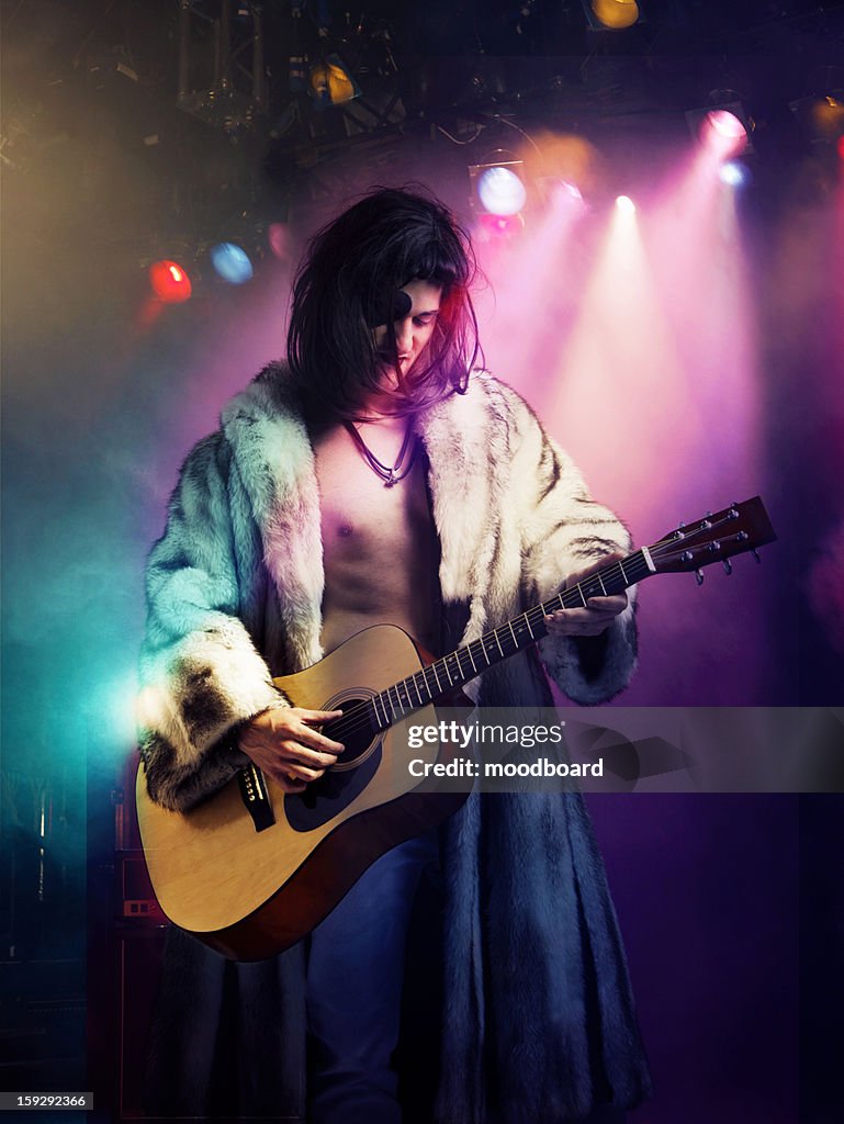 Young rock musician in fur coat playing guitar at concert