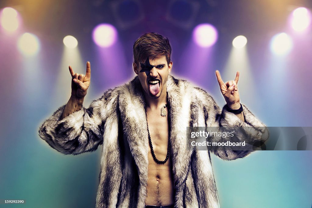 Portrait of young man in fur coat making rebellious hand gestures in rock concert