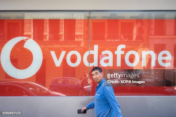 Pedestrian walks past the British multinational telecommunications corporation and phone operator, Vodafone, store and logo in Spain.