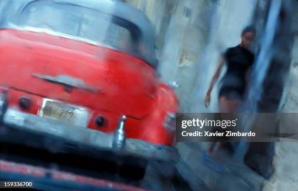 Young woman walking under rain with a red vintage car on April 27, 2001 in the street at Habana, Cuba.