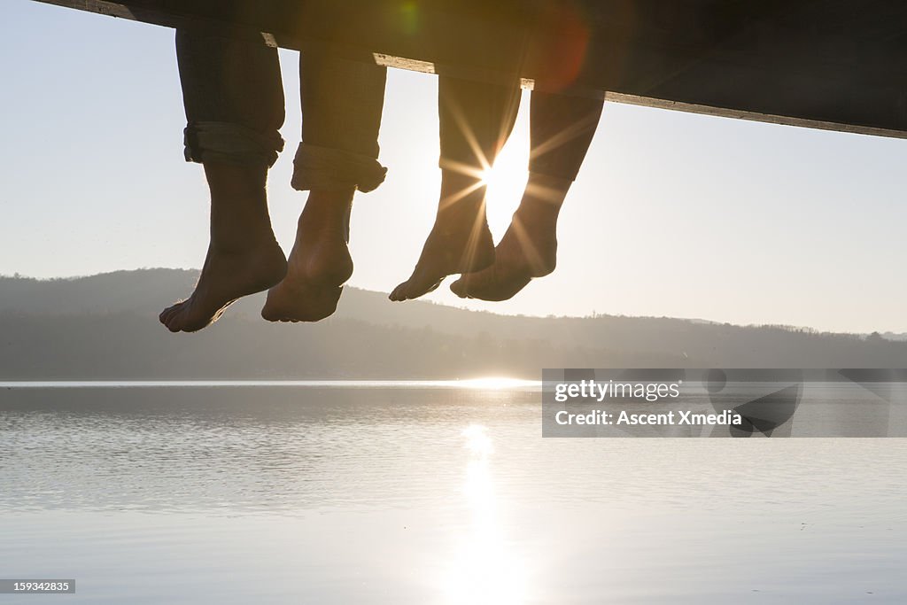 Couple's feet dangle from dock,above tranquil lake
