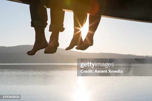 Couple's feet dangle from dock,above tranquil lake Couple's feet dangle from dock,above tranquil lake