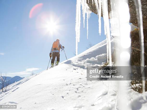 view past icicles to skier ascending slope - つらら ストックフォトと画像