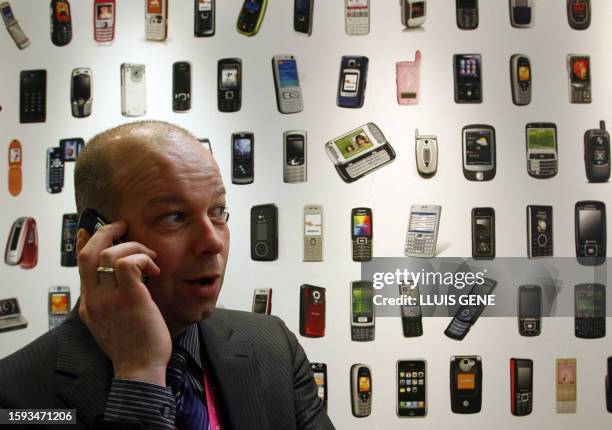 Man speaks on his phone next to a backdrop of mobile phones at the Mobile World Congress in Barcelona on February 11, 2008. AFP PHOTO/LLUIS GENE