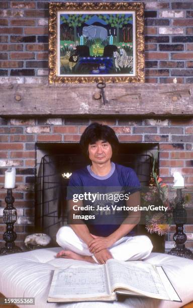 Portrait of Japanese conductor Seiji Ozawa as he sits crossed-legged on a cushion in front of a fireplace at his home, Lenox, Massachusetts, August...