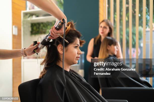 hairdresser using an electric curling iron with a client - kapsalon stockfoto's en -beelden