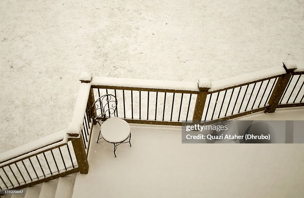 Snow covered deck with black iron chair