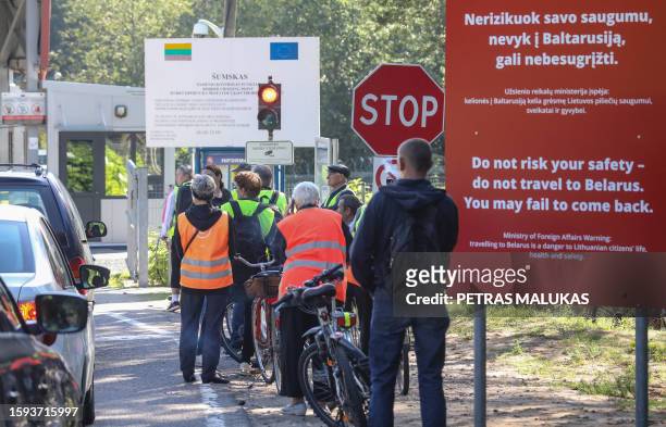 People with bicycles stand at the border crossing point Sumskas between Lithuania and Belarus on August 12, 2023 next to a sign reading "Do not risk...