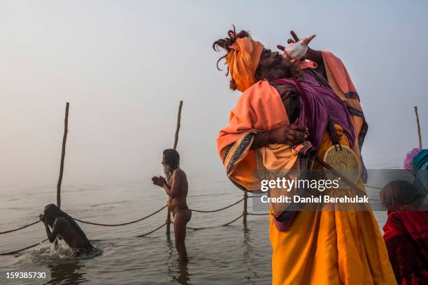 Sadhu blows a conch shell as other Sadhus or Hindu holy men bathe on the banks of the Ganges river during a procession ahead of the Maha Kumbh Mela...