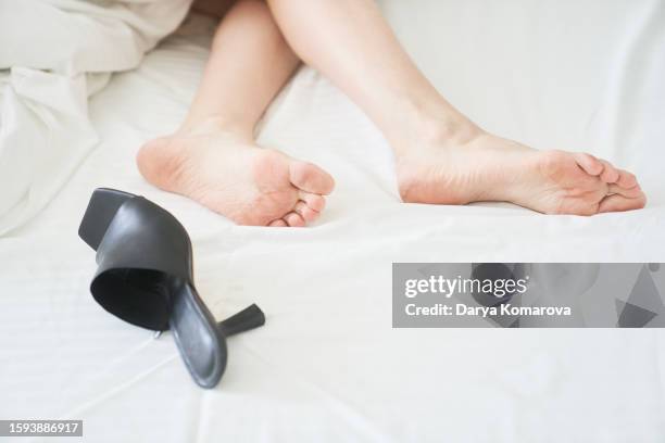 the woman's feet are under the blanket on the bed. white sheet and duvet cover. unrecognizable woman sleeping at the hotel with black heeled shoes lying on a sheet. the concept of an after-party mess. copy space. - lying on side stock pictures, royalty-free photos & images