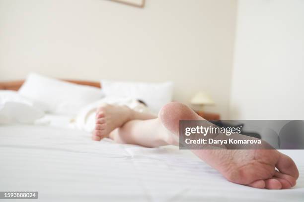 close up of the woman's foot is under the blanket on the bed. white sheet and pillows. sleep at the hotel. copy space. - woman lying on stomach with feet up stock pictures, royalty-free photos & images