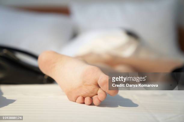 close up of the woman's foot is under the blanket on the bed. white sheet and pillows. sleep at the hotel. copy space. - woman lying on stomach with feet up stock pictures, royalty-free photos & images