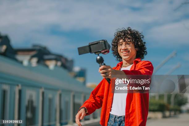 influencer asian malay generation z young man vlogging in kuala lumpur city street sidewalk looking at camera - malay people stock pictures, royalty-free photos & images
