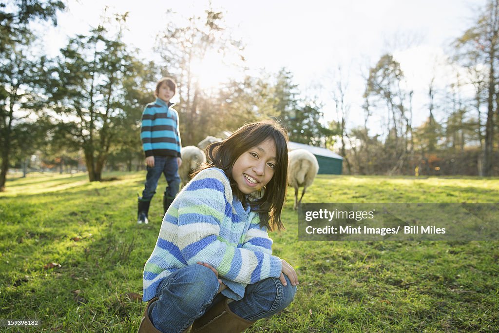 Two children at an animal sanctuary, in an animal enclosure with a group of sheep. 