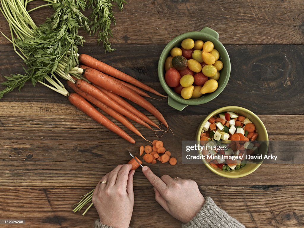 A person preparing fresh vegetables on a wooden table.