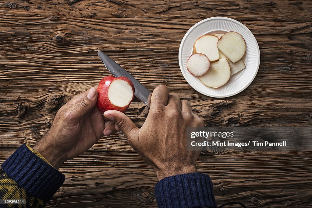 A person holding and slicing sections of a red skinned apple.