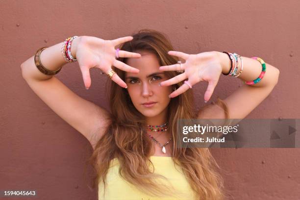 mujer joven hace gestos expresivos con sus manos delante de una pared coloreada - gestos stock-fotos und bilder