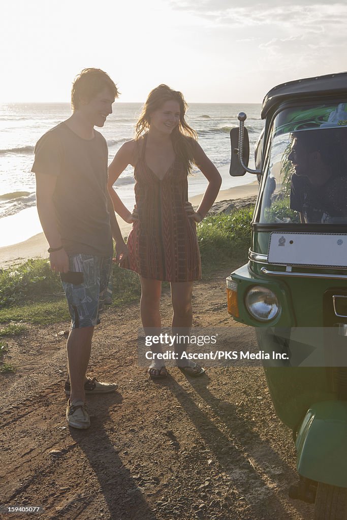 Young couple talk to tuk-tuk driver, surf behind