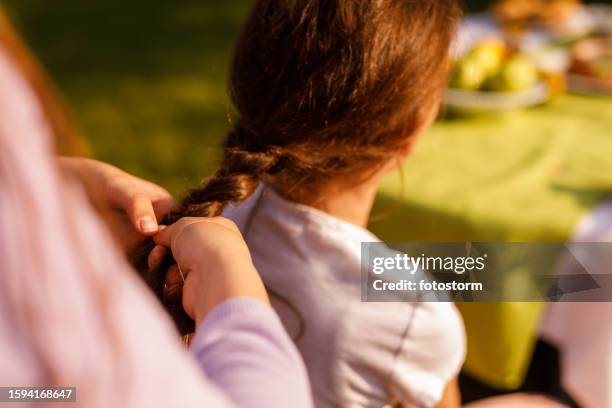 kleines mädchen flechtet die haare ihrer schwester, während sie sich in der sonne in ihrem garten entspannen - geflochten stock-fotos und bilder